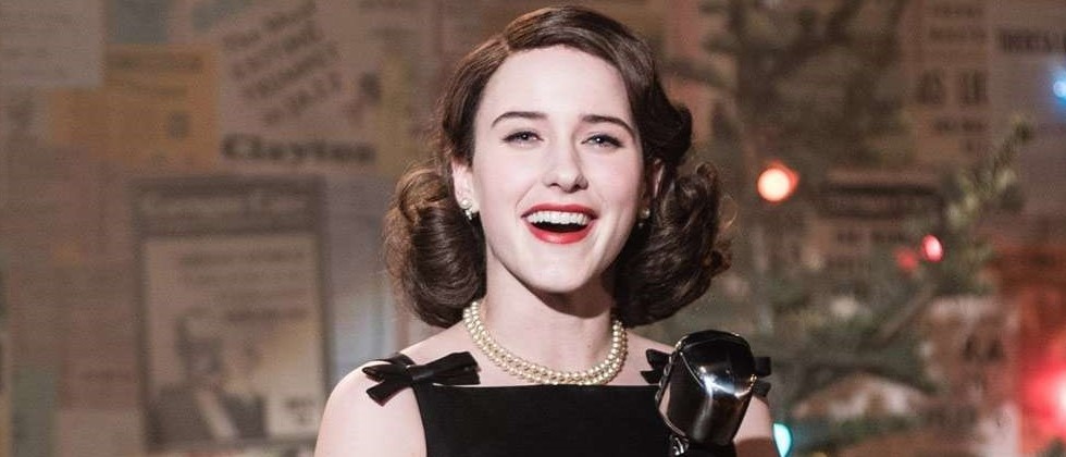 Miriam Maisel sorrindo segurando um microfone