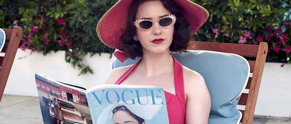 Miriam Maisel sentada lendo uma revista Vogue