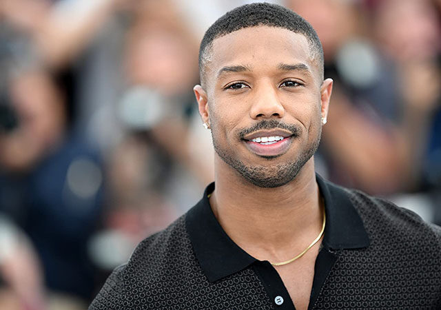 Michael B. Jordan em um evento, de camisa preta e sorrindo