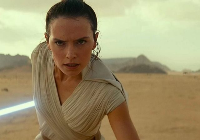 Protagonista de Star Wars olha para a câmera com semblante sério, segura seu sabre de luz e veste roupa bege